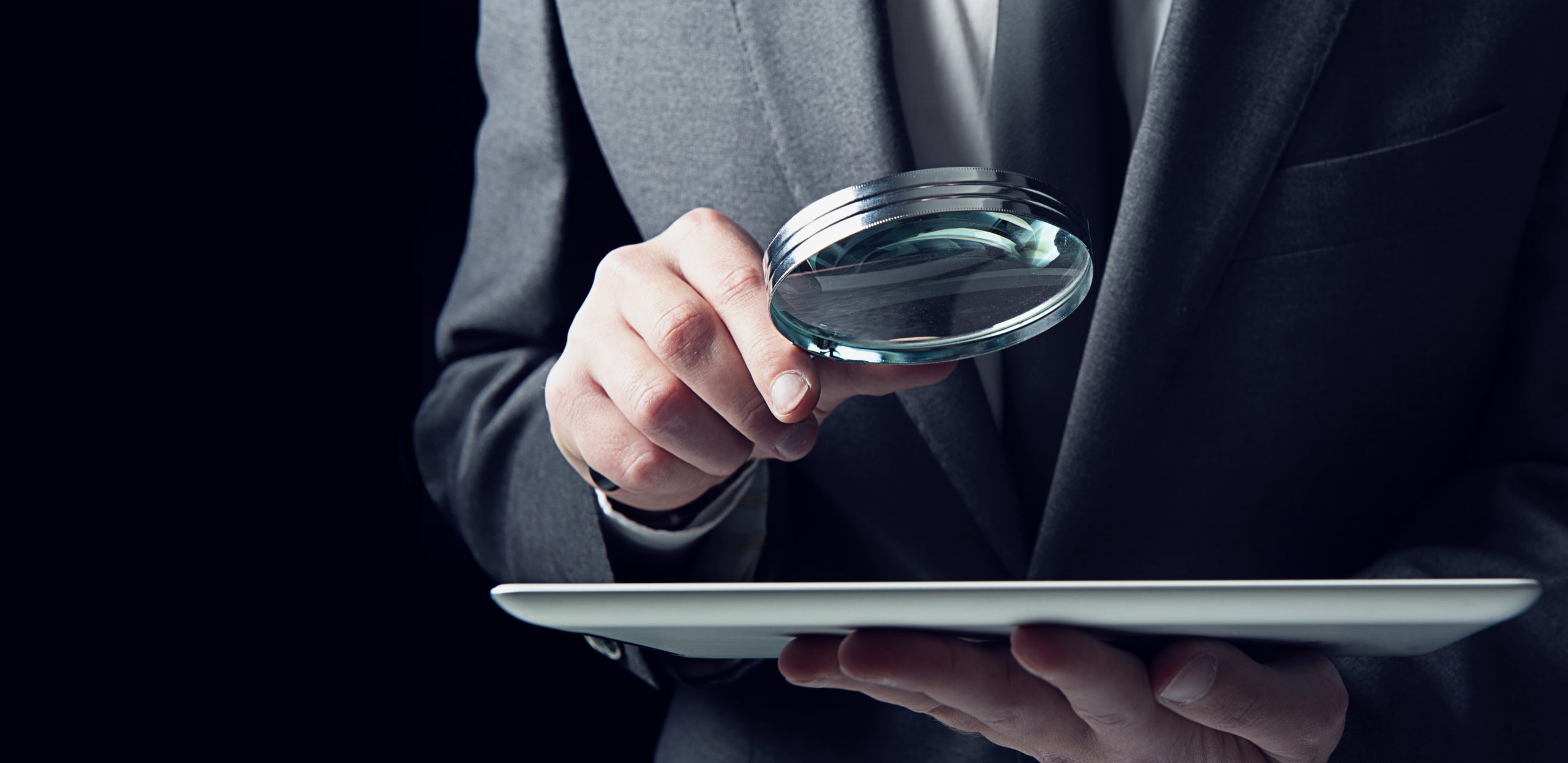 News Man in suit holding magnifying glass looking at tablet